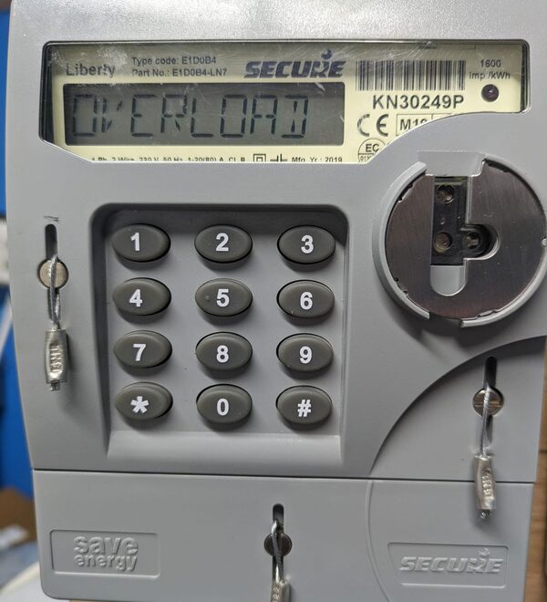 A close-up of a Secure Liberty prepayment electricity meter displaying 'OVERLOAD' with a keypad and key slots