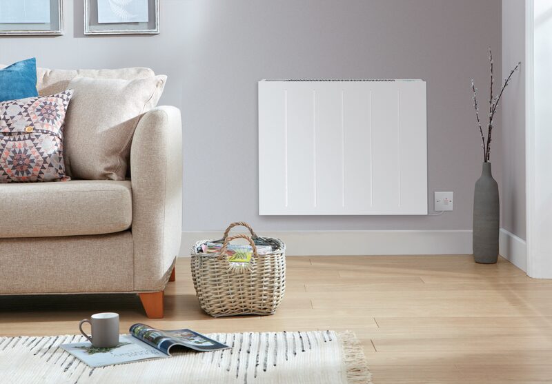 A white electric panel heater mounted on a grey wall in a living room with a sofa, basket and rug