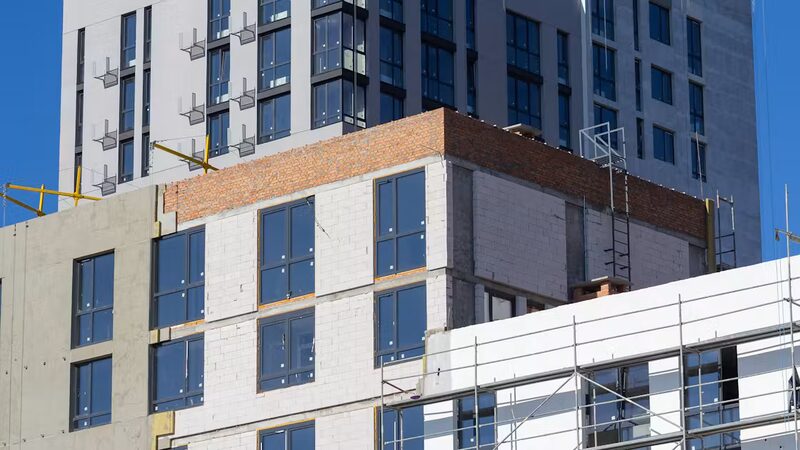 A multi-storey building under construction with external wall insulation boards and scaffolding on its facade