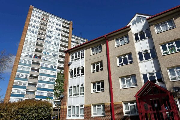 A tall residential tower block and a lower block of social housing flats under a blue sky