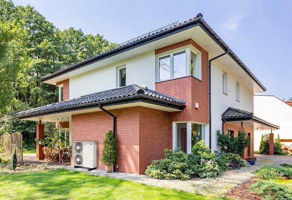 An air source heat pump unit installed outside a modern brick house with a garden