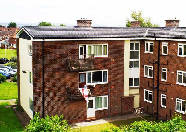 A brick block of flats with a new dark tiled roof, chimneys and balconies