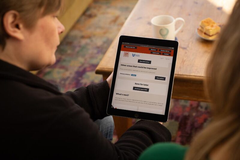 A Home Energy Scotland advisor showing an energy advice report on a tablet to a householder at a table