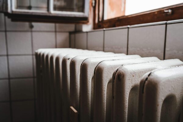 An old white cast-iron radiator against tiled walls under a window in a dim room
