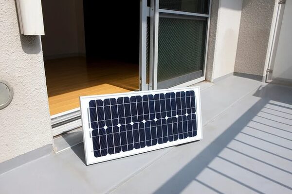A single solar panel leaning against a sliding glass door on a flat balcony