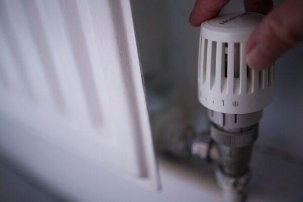 A hand turning the thermostatic radiator valve dial on a white radiator