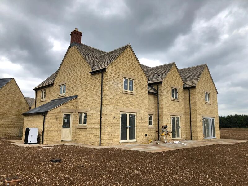 A newly built Cotswold stone house with a heat pump unit installed at the side of the property