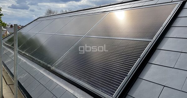 In-roof solar PV panels integrated into a slate roof on a house, with the sun reflecting off the glass