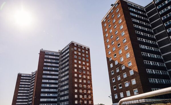 Tall brick residential tower blocks seen from below against a bright sunny sky