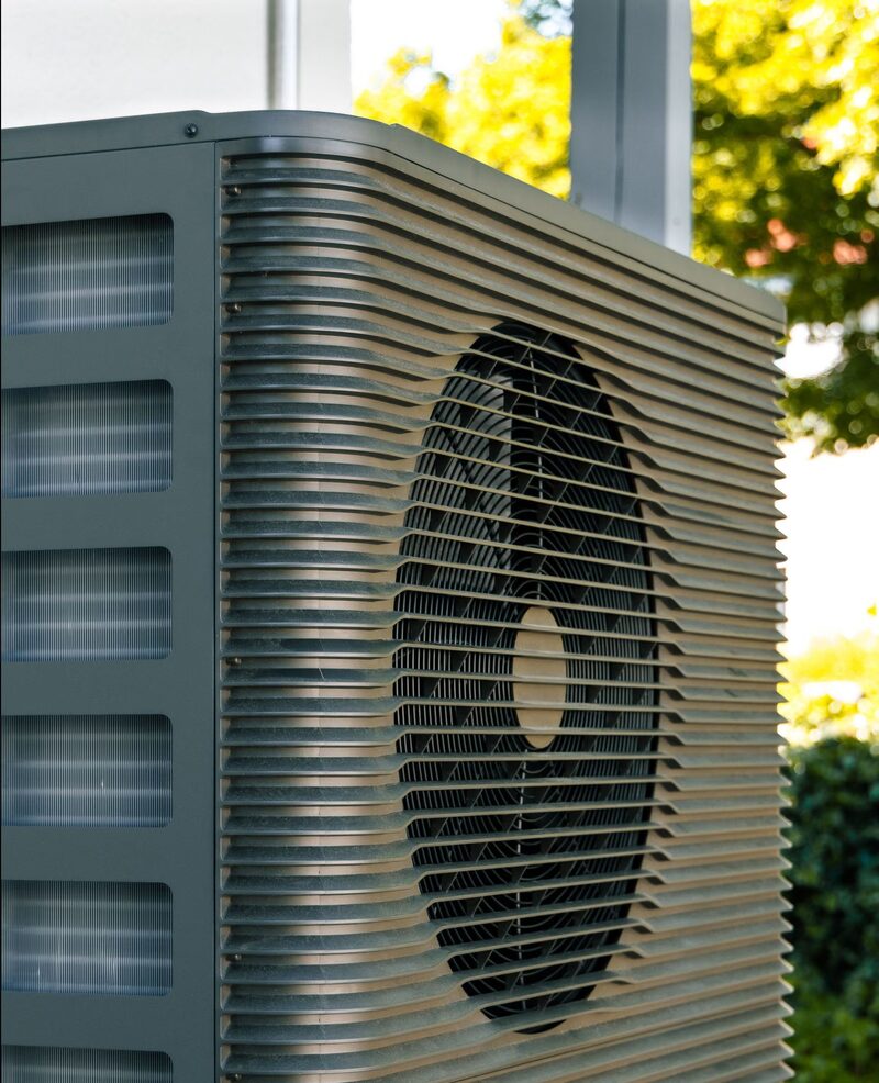 A close-up of an outdoor air source heat pump unit with a fan grille, installed outside a house