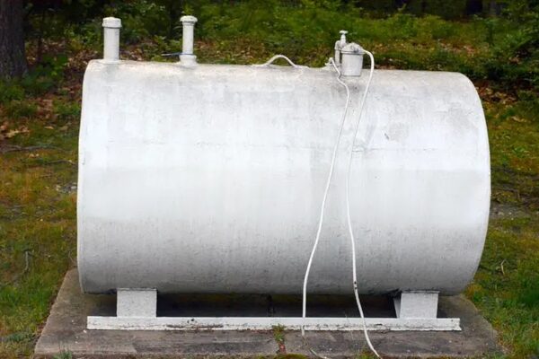 A large white cylindrical oil tank standing on a concrete plinth in a grassy garden