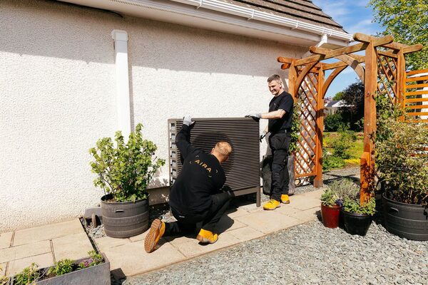 Two Aira engineers installing an air source heat pump unit outside a house in a garden