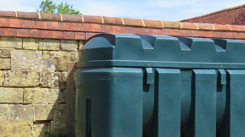A green plastic heating oil tank installed against a stone wall with a tiled roof behind it