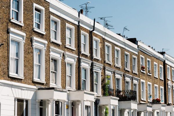 A row of traditional English brick terraced houses with white window frames and TV aerials on a sunny day