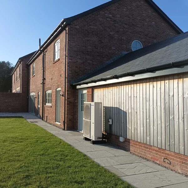 An air source heat pump unit installed outside a brick house next to a timber-clad garage