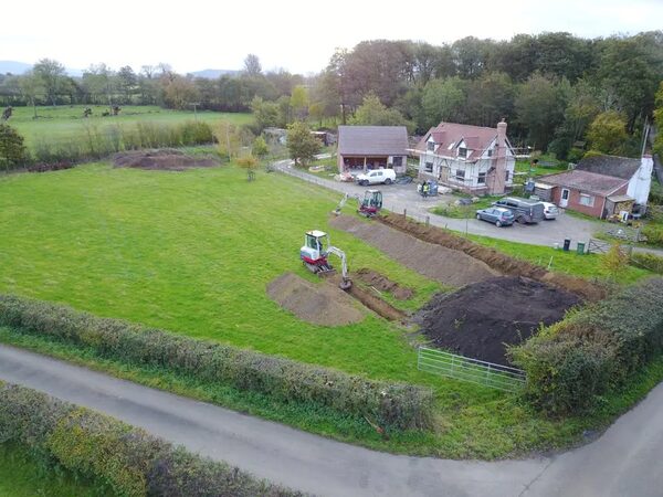 Aerial view of a rural cottage garden with a mini digger excavating a trench for a ground source heat pump ground loop