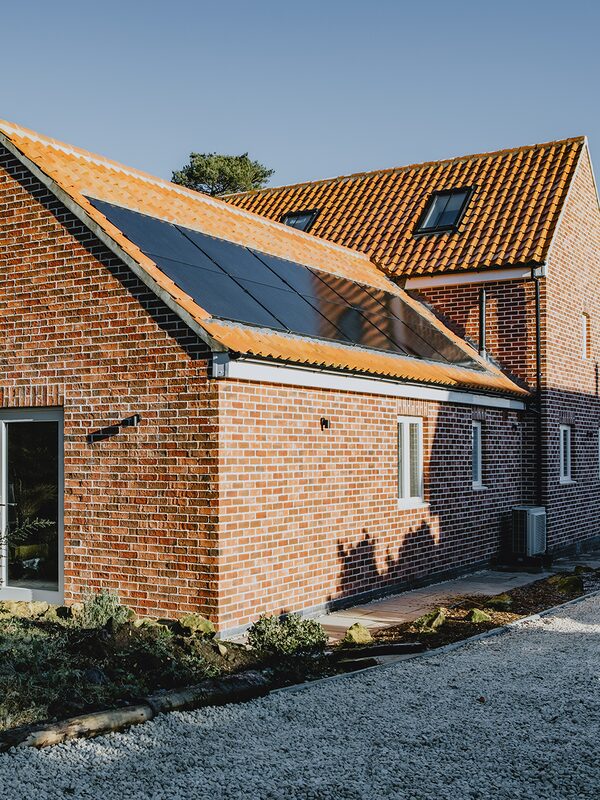 A brick house with solar panels on the tiled roof and an air source heat pump unit on the outside wall