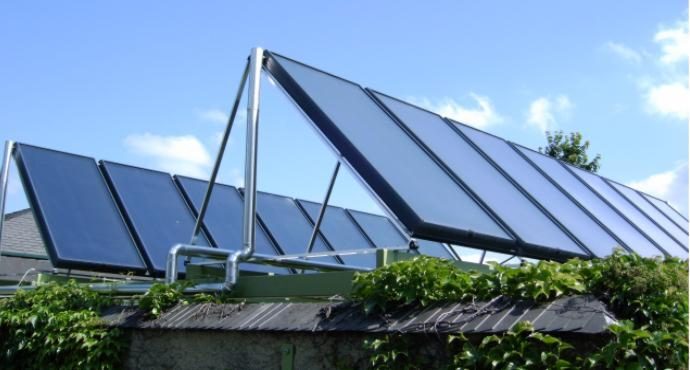 A rack-mounted field of flat-plate solar thermal collectors installed on a flat roof with ivy-covered walls