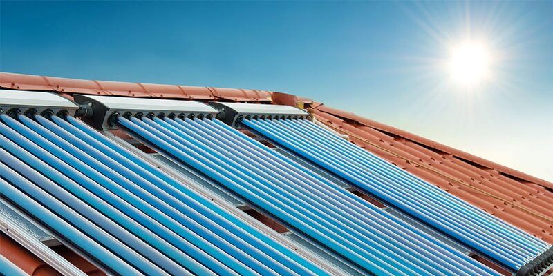 Evacuated-tube solar thermal collector panels installed on a terracotta tiled roof under a bright sun