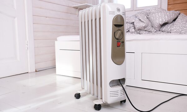 A white portable oil-filled radiator with control dial and power lead standing on castors in a bright bedroom
