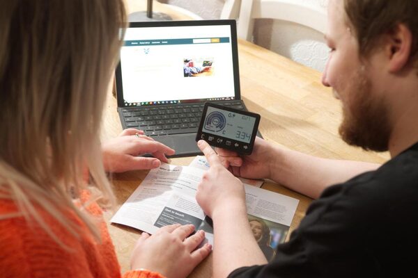 An advisor showing a woman how to use a smart meter display at a table with a laptop and leaflets
