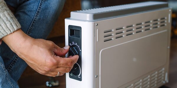 A person adjusting the thermostat dial on a white portable electric convection heater