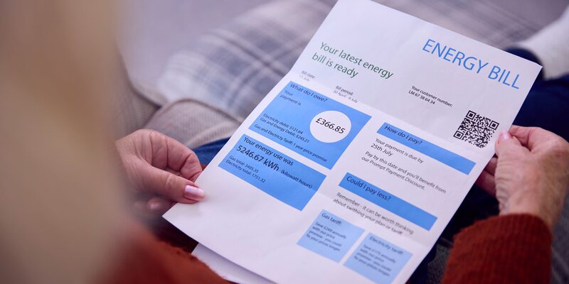 A person holding and reading a printed energy bill showing amounts due and energy usage