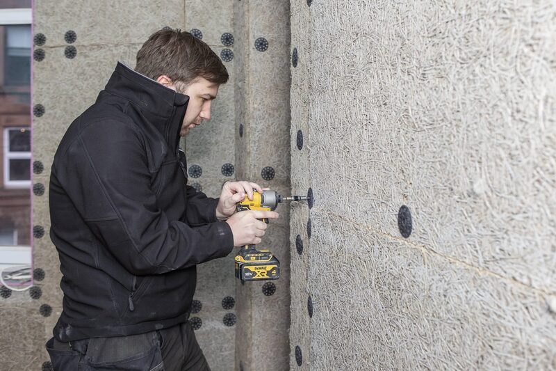 An installer using a DeWalt cordless drill to fix internal wall insulation boards with washers in a room