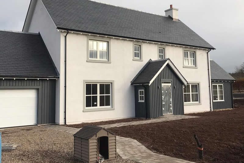 A large modern white and grey Scottish house with a newly completed air source heat pump installation, with a small pump enclosure in the garden