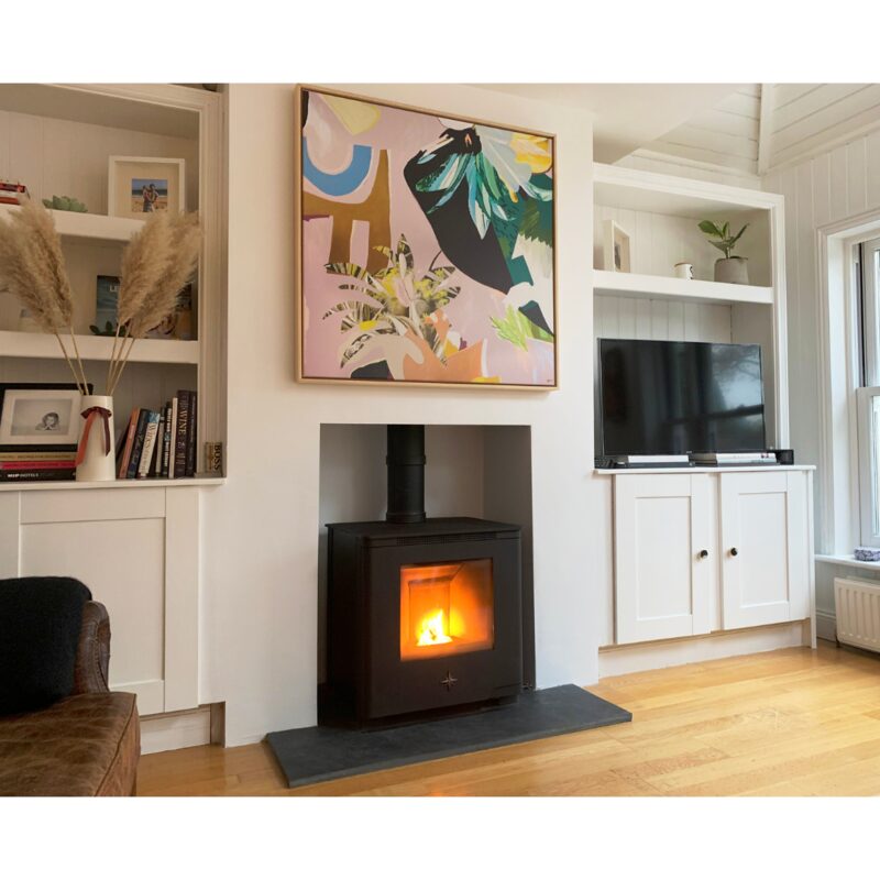 A black wood-burning stove with a lit fire installed in a fireplace in a bright living room