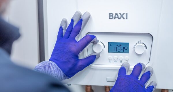 A gloved engineer adjusting the controls of a white Baxi combi gas boiler