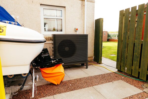 An Aira air source heat pump installed on the outside wall of a house next to a boat on a trailer