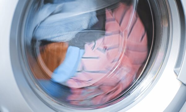 Clothes tumbling inside the drum of a tumble dryer, seen through the round glass door