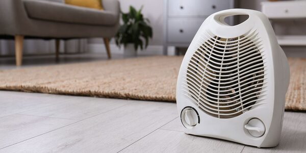 A white portable electric fan heater with control dials standing on a wooden floor in a living room