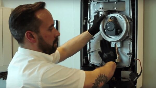 An engineer in black gloves servicing the internal components of an Intergas gas boiler with the casing removed