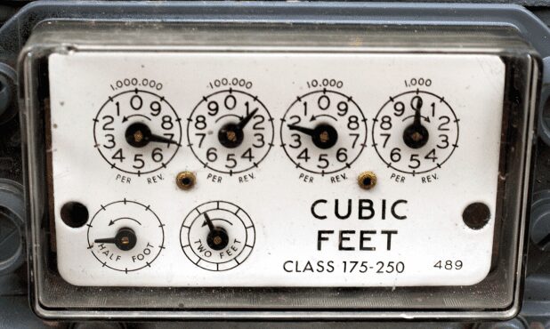 A close-up of an old dial-style gas meter face reading in cubic feet