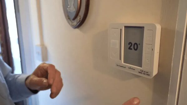 A person adjusting a white wall-mounted Honeywell digital room thermostat set to 20 degrees