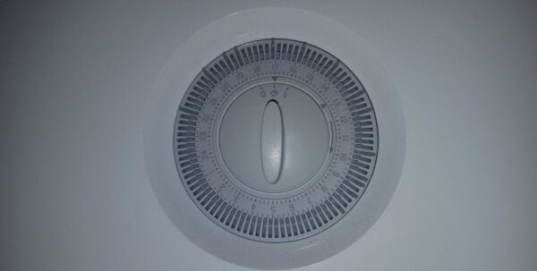 A close-up of a round mechanical 24-hour heating timer dial with hour tappets, mounted on a wall