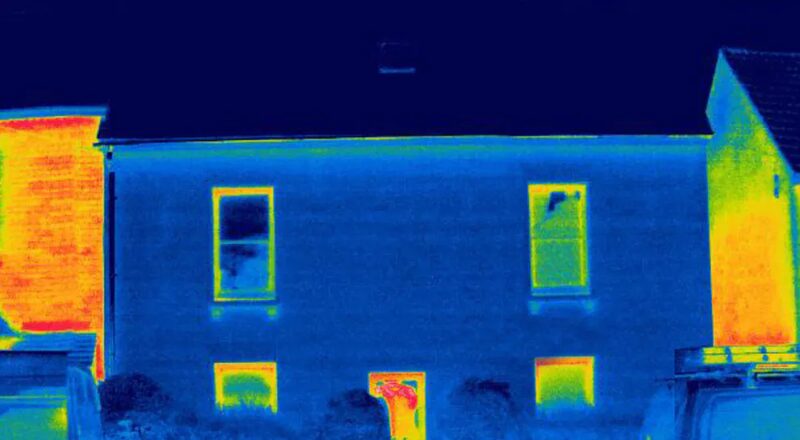 A thermal imaging photograph of a two-storey house showing heat loss around windows and doors