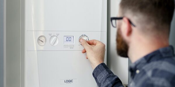 A man adjusting the control dial on a white Ideal Logic combi boiler with a digital display and pressure gauge