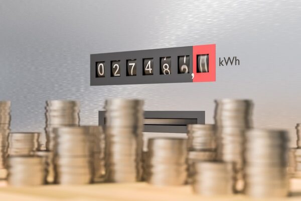A close-up of an electricity meter display reading kWh with stacks of coins in the foreground