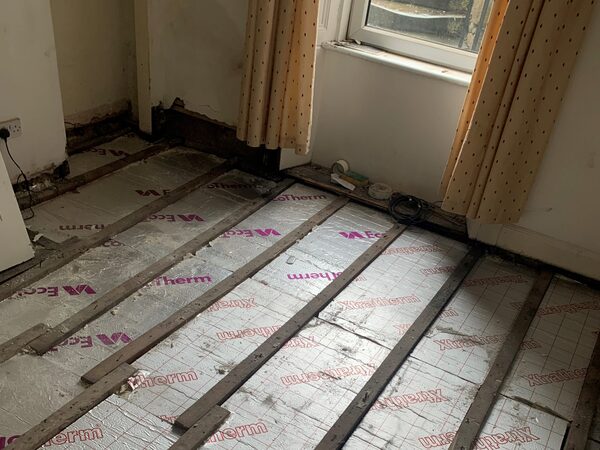 A room with floorboards removed showing Xtratherm insulation boards and timber battens being fitted for underfloor heating installation