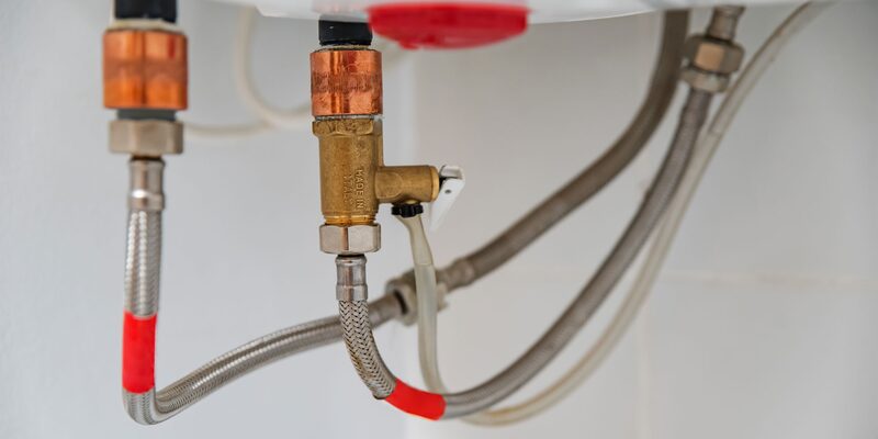 Close-up of copper and braided steel boiler pipes and a brass valve connected to a boiler