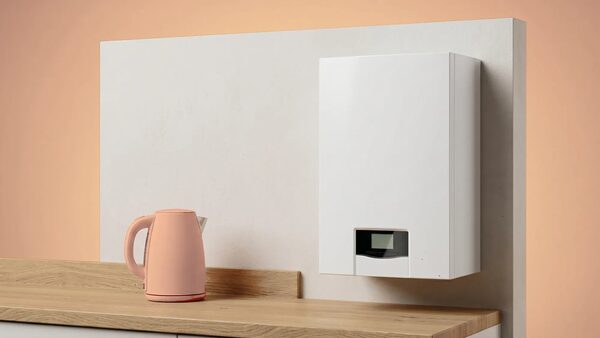 A white wall-mounted combi boiler on a kitchen wall next to a pink electric kettle on a wooden worktop