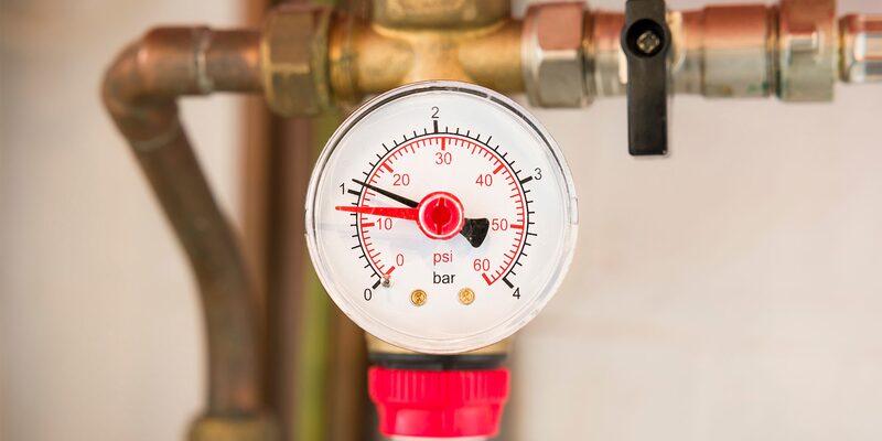 A close-up of a boiler pressure gauge reading about 1 bar, mounted on copper pipework