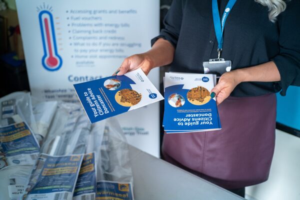 A Citizens Advice worker holding Doncaster Citizens Advice guide leaflets at an advice stand with warm home discount leaflets on a table