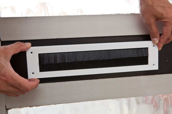 Hands fitting a white bristle brush letterbox draught excluder to a door