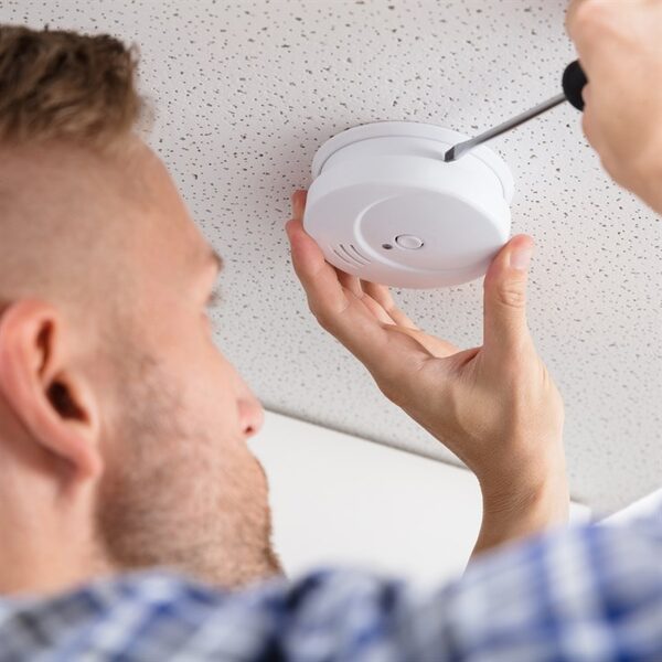 A man installing a white ceiling-mounted smoke alarm with a screwdriver