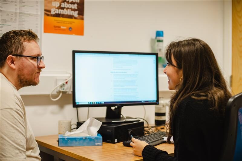 An adviser and a client talking at a desk in front of a computer monitor in an advice office