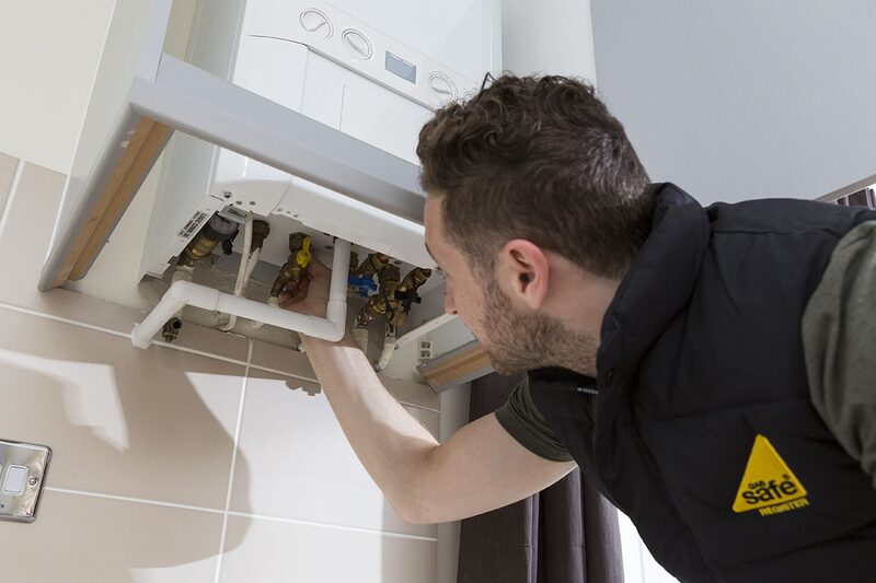 A Gas Safe registered engineer working on the pipework beneath a wall-mounted gas boiler in a home